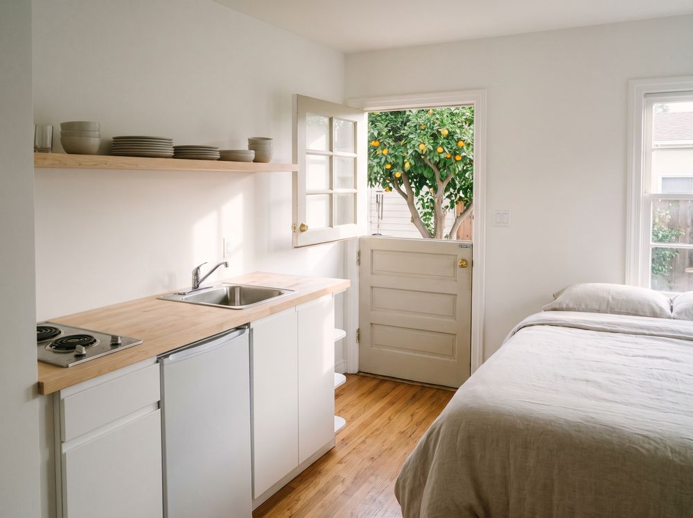 A small suite with a kitchenette along one wall, a bed and a Dutch door open to an orange tree